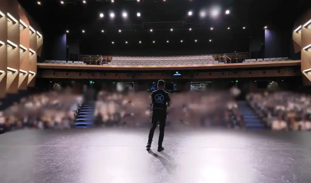 Daniel Merza presenting to senior students about mindset, motivation, and wellbeing in a school auditorium.